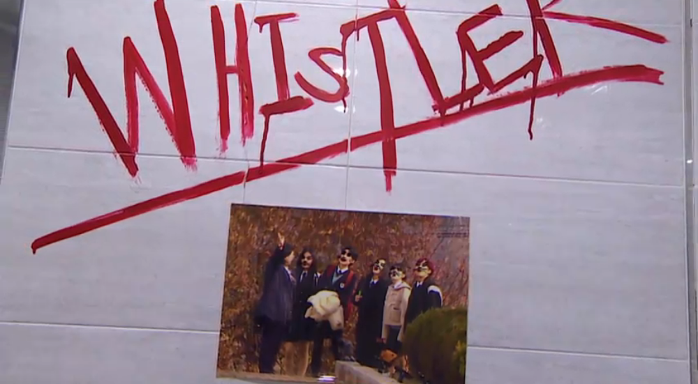 화장실 벽에 빨간색 유성 락카로 WHISTLER라고 쓰여 있으며 출연진들의 사진의 얼굴에 쥐를 덧그림.